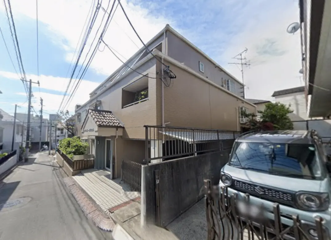 - 新しい外壁の建物と狭い路地、前方に駐車された車、周囲に電柱と電線が見える住宅街の風景