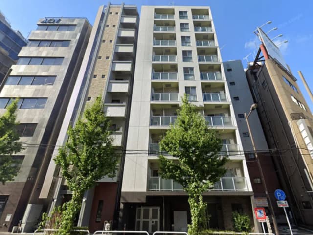 - モダンな外観のアパートメントビル、周囲に緑の木々があり、近隣のビルと共存する都市景観