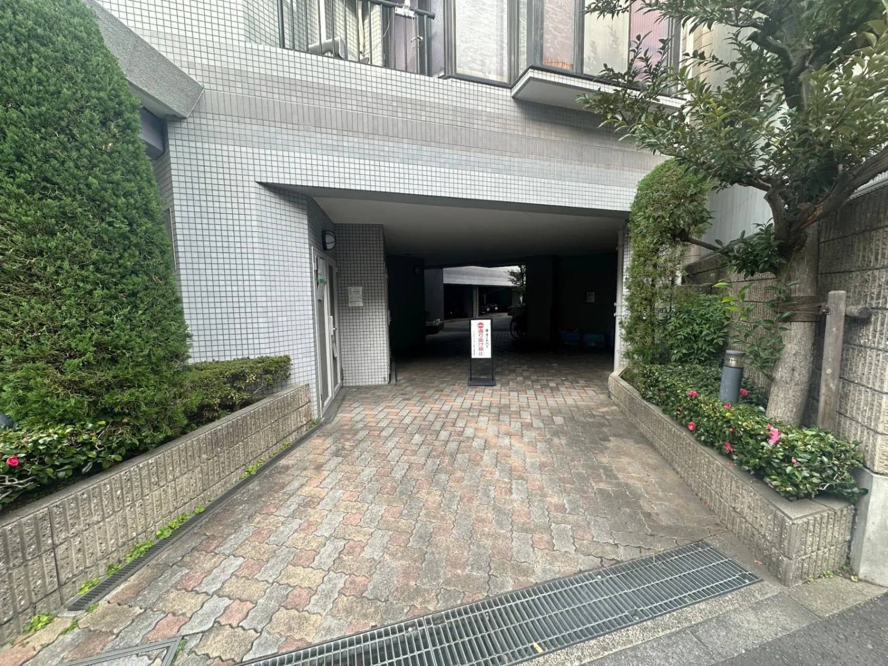 都市のマンションの入り口と駐車場、緑の植栽とタイル貼りの外観