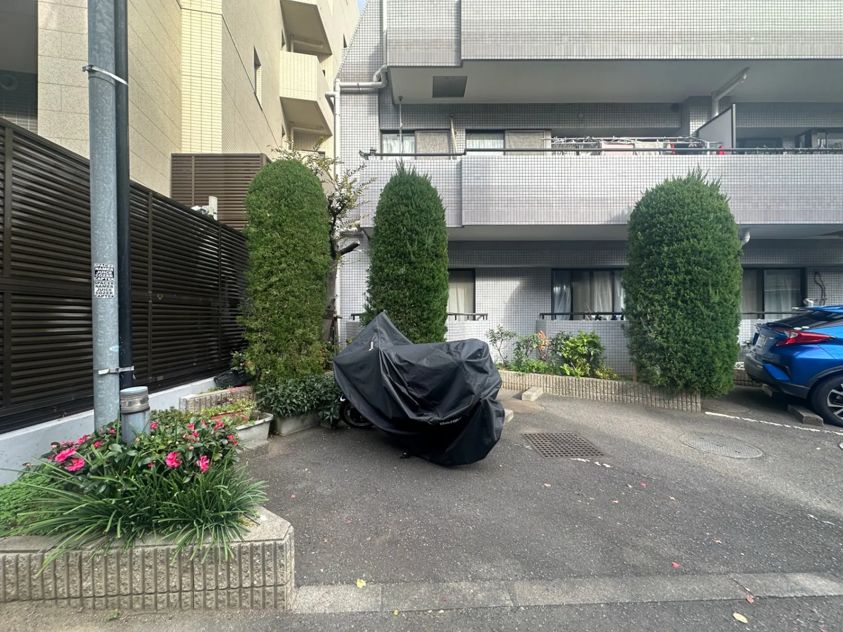 都市のマンション前の歩道、緑の植栽と花壇、カバーされたバイクと駐車している車