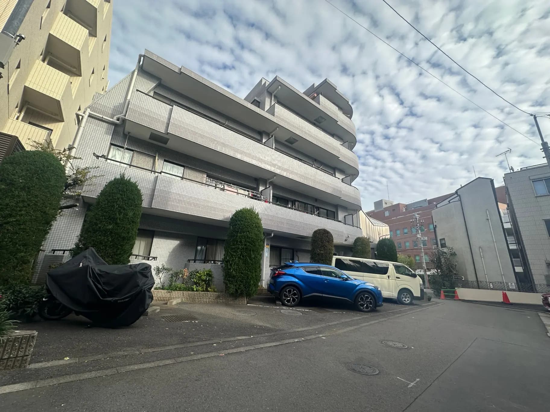 現代的なマンションの外観、晴れた日の青い空、駐車場に車が並ぶ都市の風景
