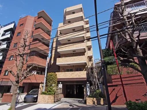 - モダンな外観のマンションビル、周囲には住宅や商業施設が立ち並ぶ都市の風景