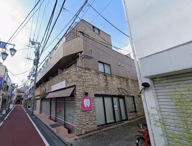 - 石造りのファサードを持つクリニックの外観、赤い道路と周囲の電線が見える商店街の風景