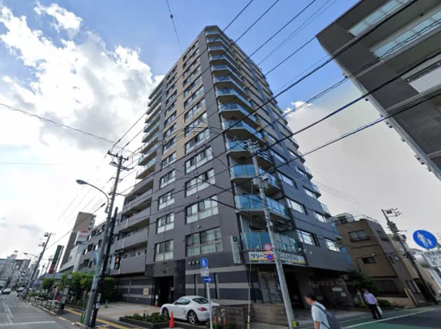 - モダンなデザインの高層マンション、外観はガラスとコンクリート、近くに歩行者と車が行き交う街並みが見える