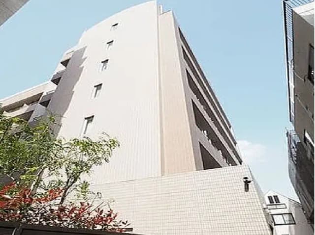 - 近代的な外観の高層ビル、周囲に植物があり淡い色合いのタイル張り、青空とともに楽しむ都市風景