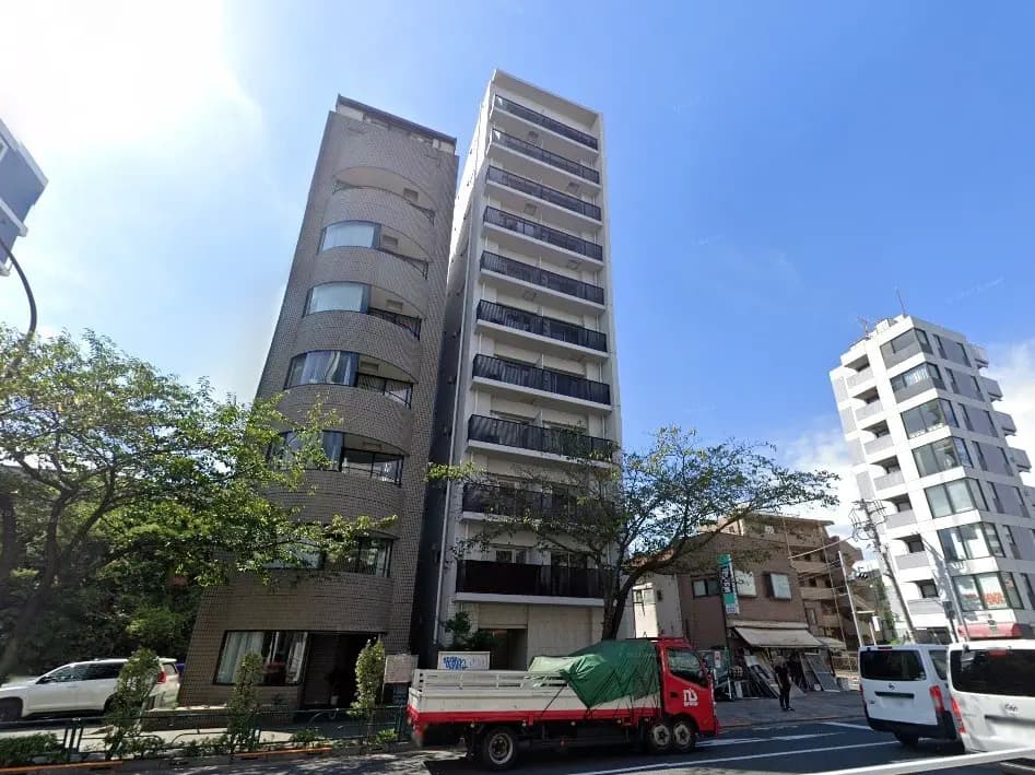 - 近代的なデザインのマンションと周辺の街並み、青空と樹木が映える都市風景