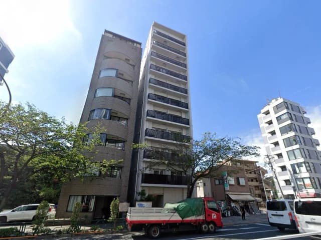 - 近代的なデザインのマンションと周辺の街並み、青空と樹木が映える都市風景