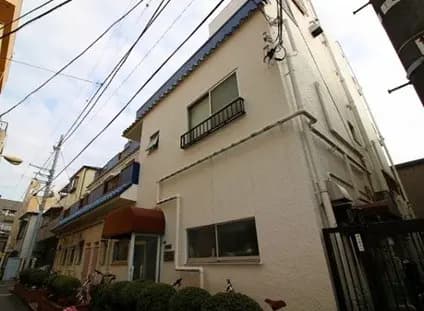 都市の住宅街にある2階建てのモダンな白い家、青い空と周囲の建物
