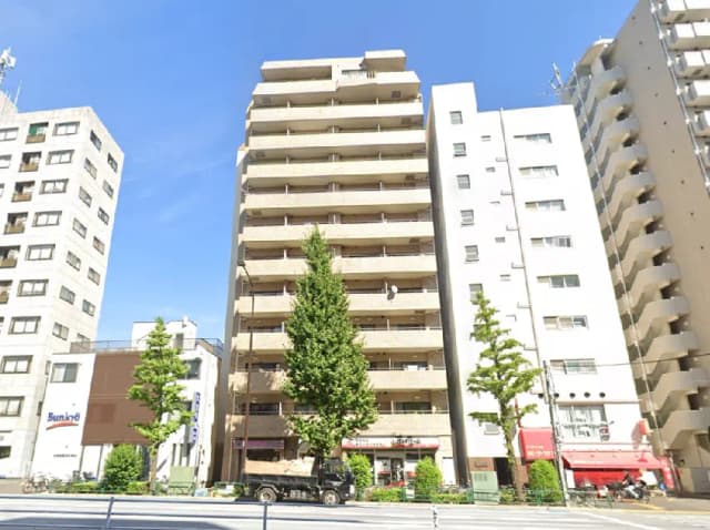 - 都心に立つ高層マンションと周囲のビル、青空と緑の木々が見える風景