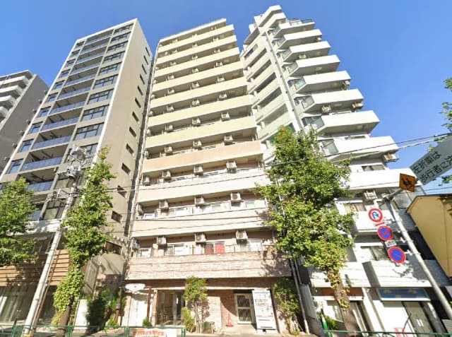 - 都市型マンションの外観、複数のエアコンユニットが設置された階段状の建物と周囲の緑豊かな街並み