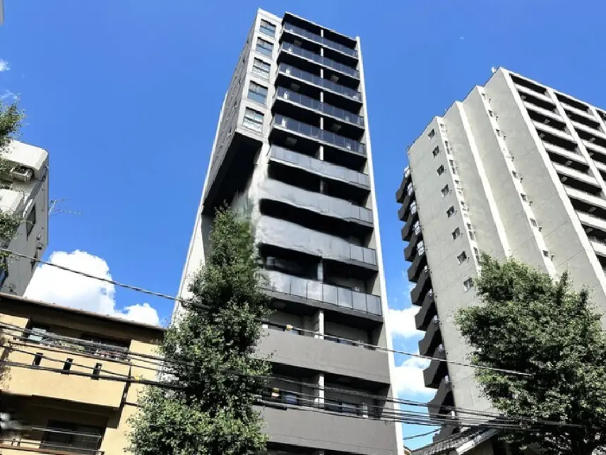- 青空を背景にした現代的な高層マンション、左側には緑の木があり、周囲の建物と共に都市の風景を形成している
