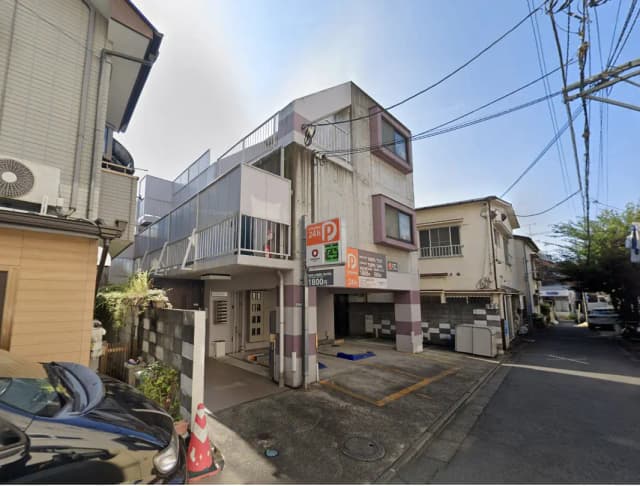 - コンクリート製のビルと駐車場、周囲に住宅が並ぶ閑静なストリートの風景、晴れた青空の下での外観