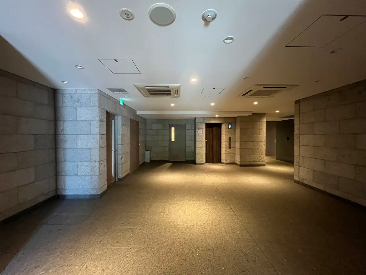 - モダンなデザインのロビー、石材の壁と温かみのある照明、エレベーターとドアが並ぶ落ち着いた雰囲気の空間