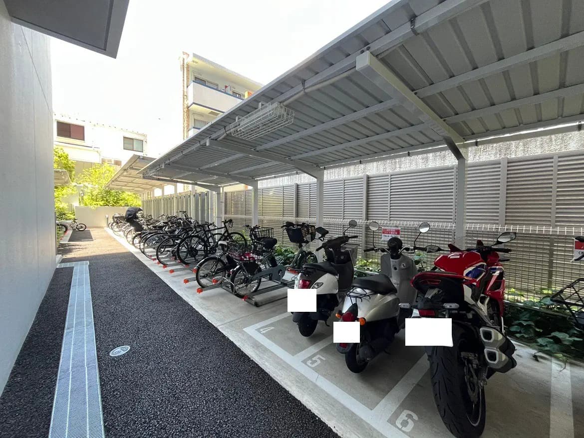 - 自転車とバイクが整然と並ぶ屋根付きの駐輪場、周囲には緑が見える快適なスペース