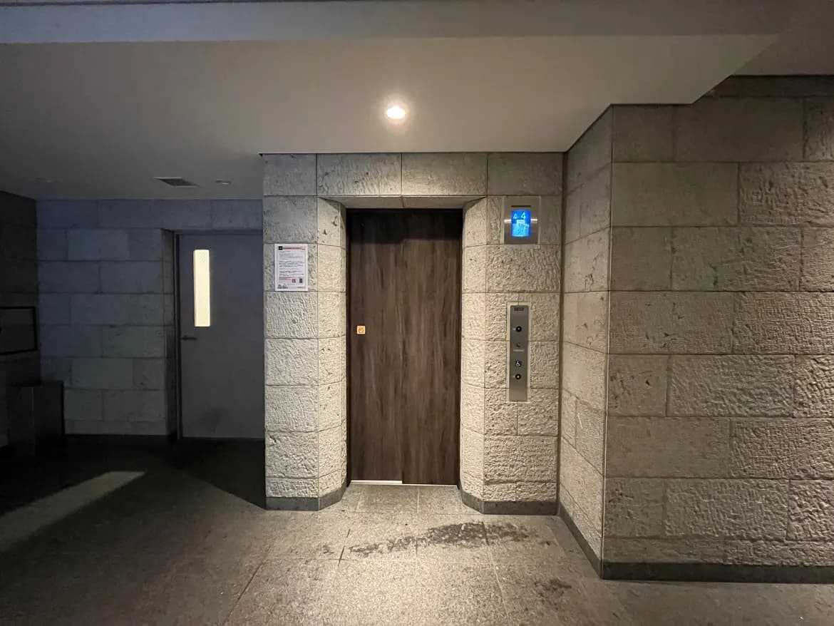 - モダンな建物のエントランス、木製のドアとエレベーターが配置された石造りの内装、明るい照明のシーン