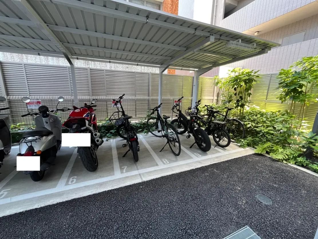 - 自転車とバイクが並ぶ屋根付きの駐輪場、緑の植物が周囲に配置された清潔感のある空間
