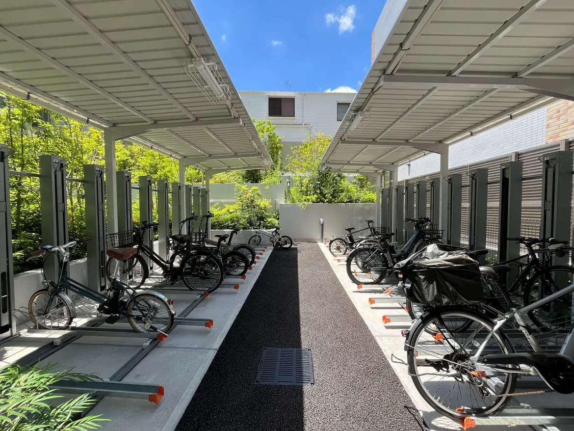 - 自転車専用の屋根付き駐輪場、整理された自転車と緑の植栽がある明るい環境の風景