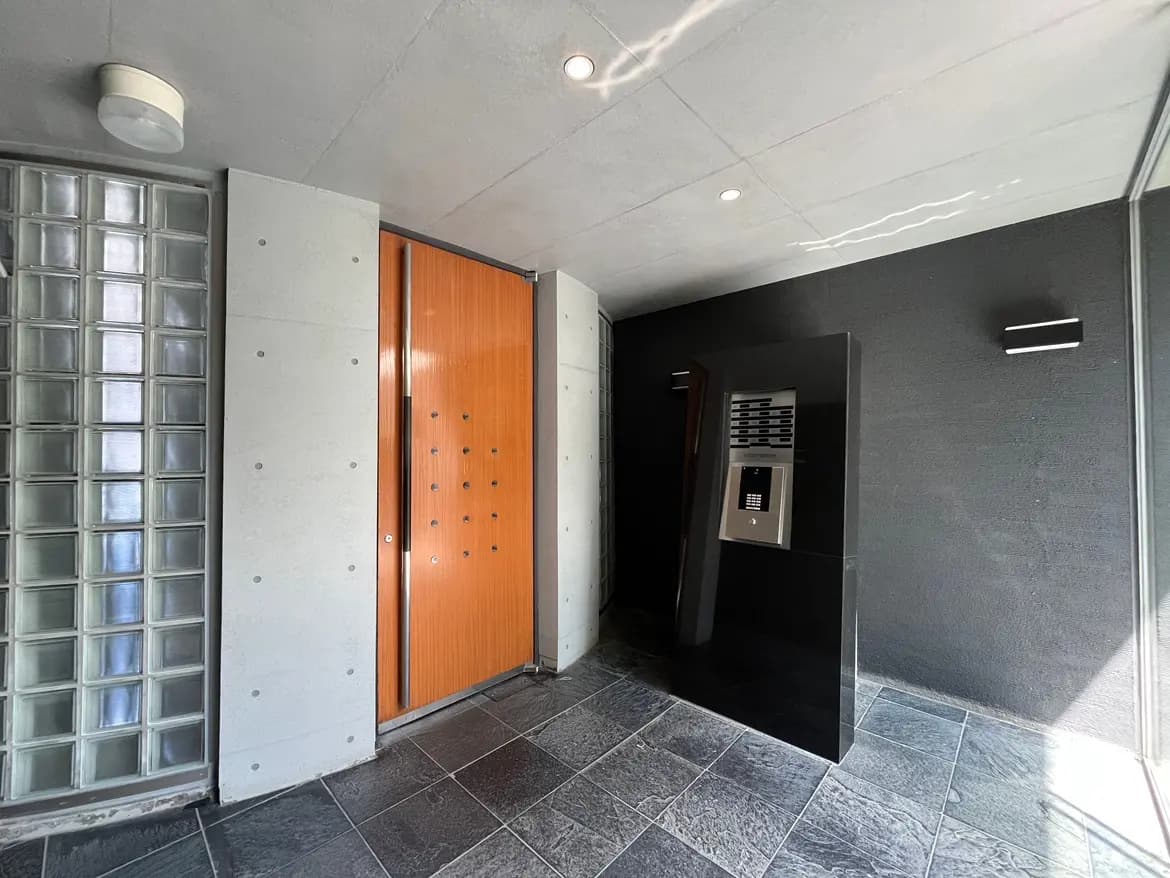 - モダンなエントランスホール、ガラスブロックの壁と木製の玄関ドア、スタイリッシュなインターホンと照明のあるシンプルな内装デザイン