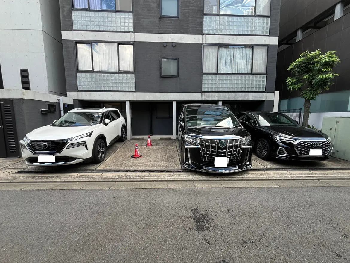 - 都市の駐車場に停車している3台の車、左から日産のSUV、トヨタの高級車、アウディのセダン、背景にはモダンな建物が見える風景