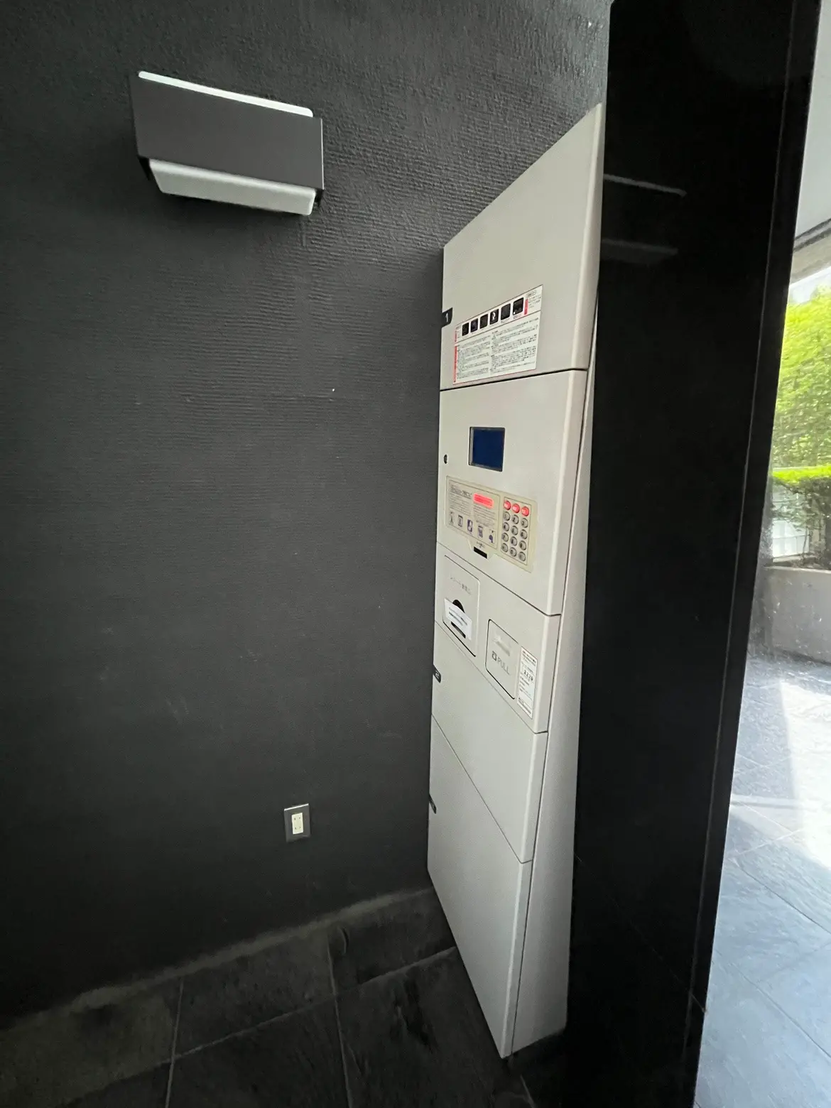 - モダンなデザインのエントランスに設置された宅配ボックス、黒い壁に囲まれたシンプルな外観