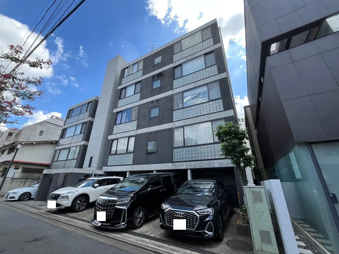 - 現代的な外観のアパートメントビルと駐車場に並ぶ高級車、青空と雲が広がる日中の風景