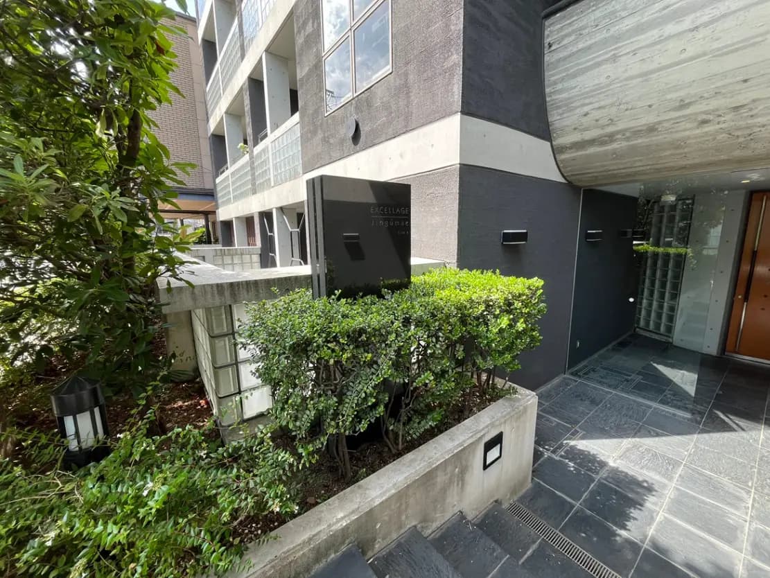 - モダンな外観のマンションエントランス、緑豊かな植栽と洗練されたデザインの照明が配されたアプローチ