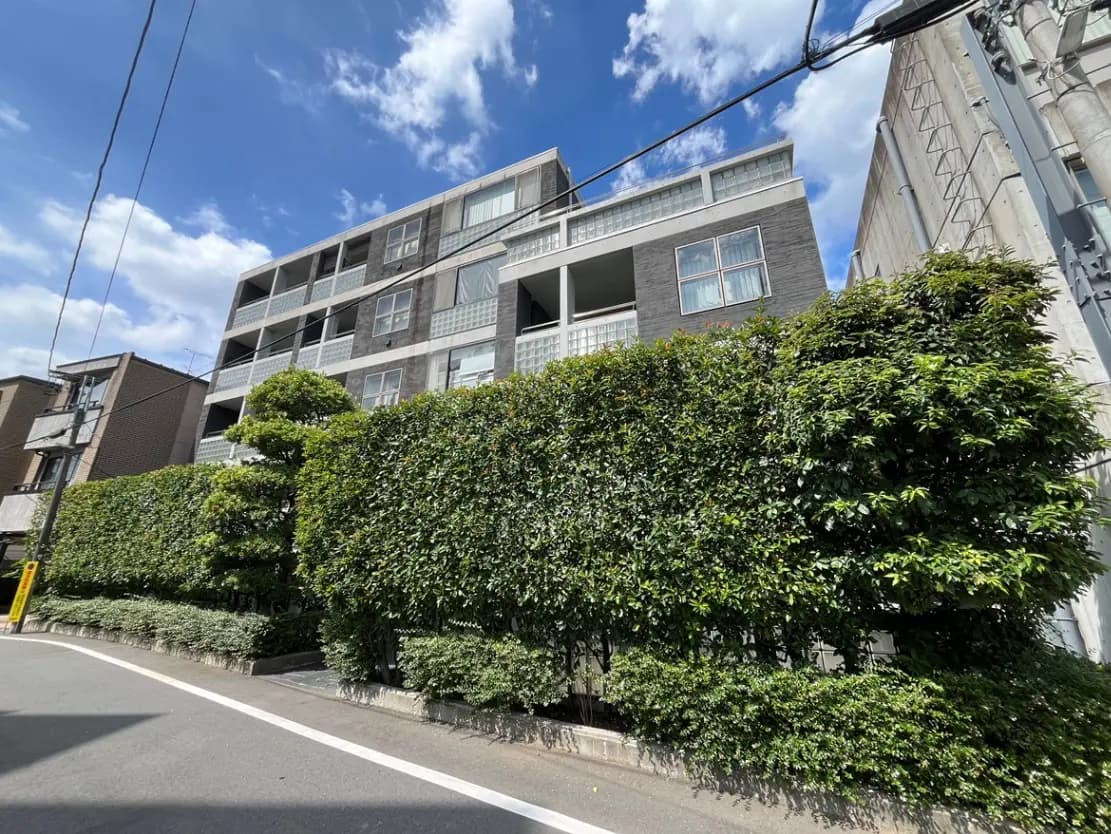 - モダンな外観の住宅ビル、周囲の緑豊かな植栽と青空の対比が印象的な風景