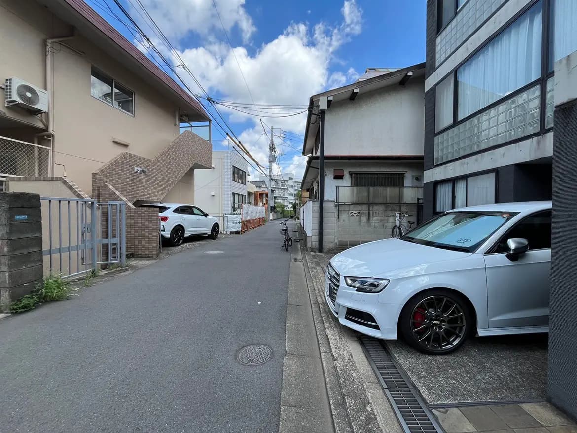 - 駐車スペースに停まった白いスポーツカーと住宅街の風景、青空と雲が広がる午後の光景