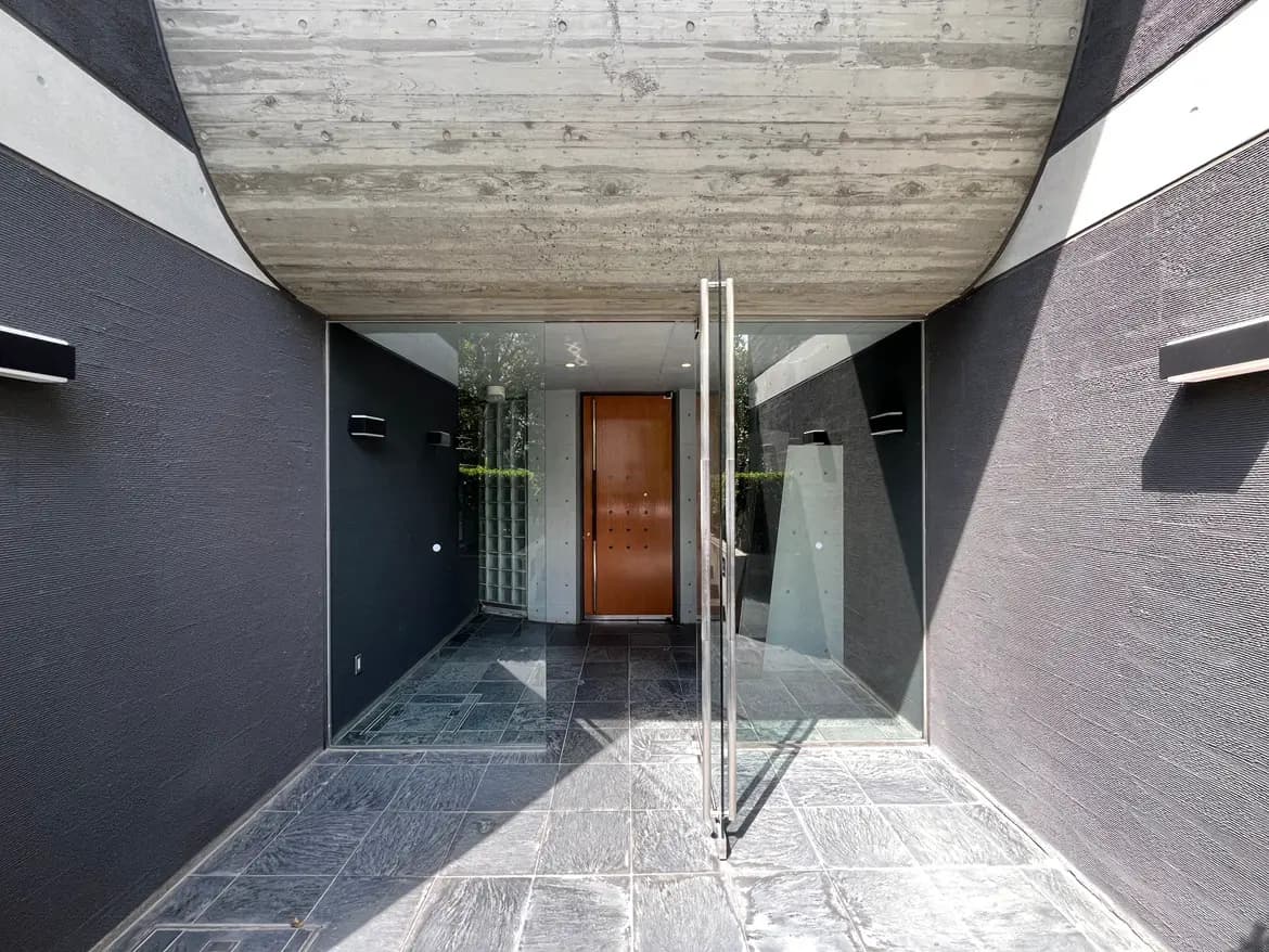 - モダンなデザインのエントランス、ガラス扉と木製ドア、コンクリートの天井、シンプルな黒い壁の仕上げ