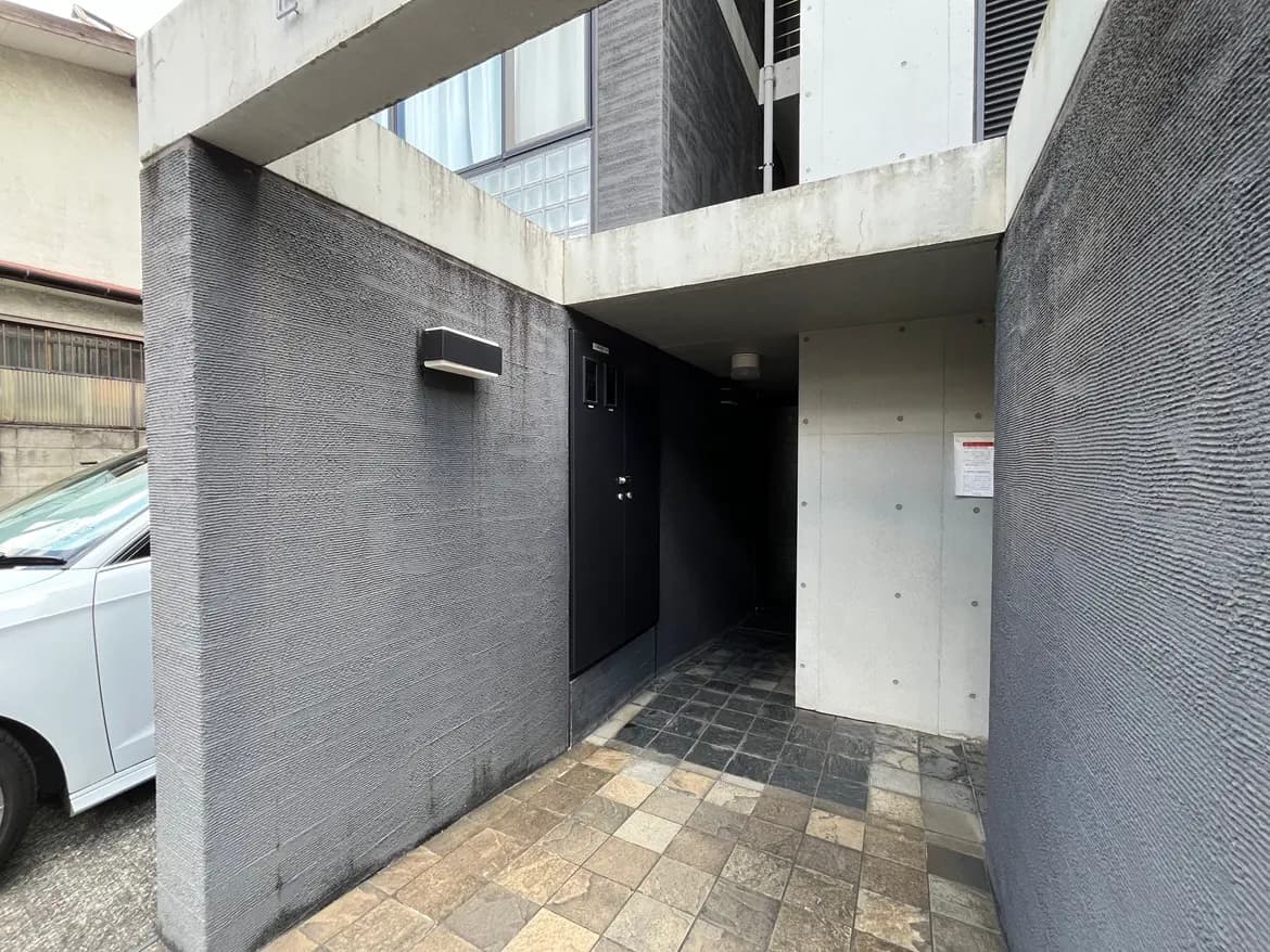 - モダンなデザインの住宅エントランス、コンクリートと石材の床、暗色のドアが特徴的な外観