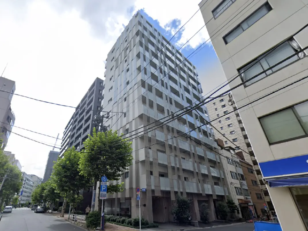 - モダンな外観のアパートメントビル、周囲には緑豊かな樹木と電柱、晴れた青空が広がる街並み