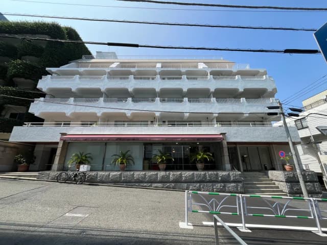 - 白い外壁のモダンな建物、テラス付きのバルコニーが特徴、日本の都市の街並みに溶け込むデザイン