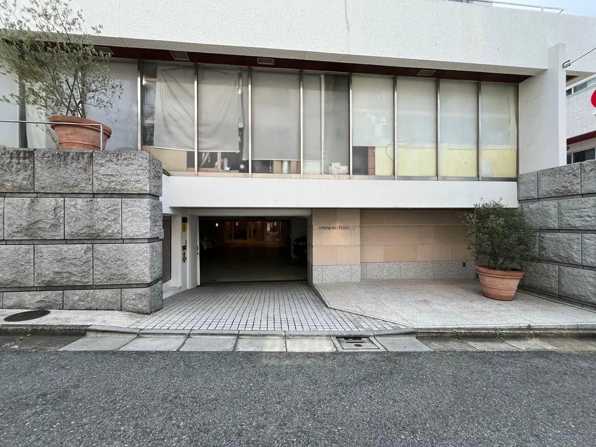 - 表参道に位置する現代的な建物の外観、ガラスの壁と石造りのエントランス、観葉植物が置かれたアプローチ