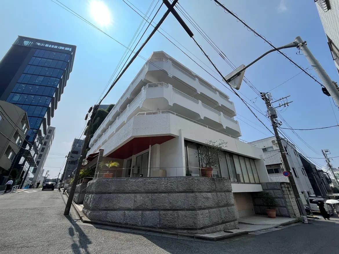 - 近代的な建物が並ぶ街並みの中、白い外壁のマンションと周囲のビル、明るい空と交通信号が映る風景