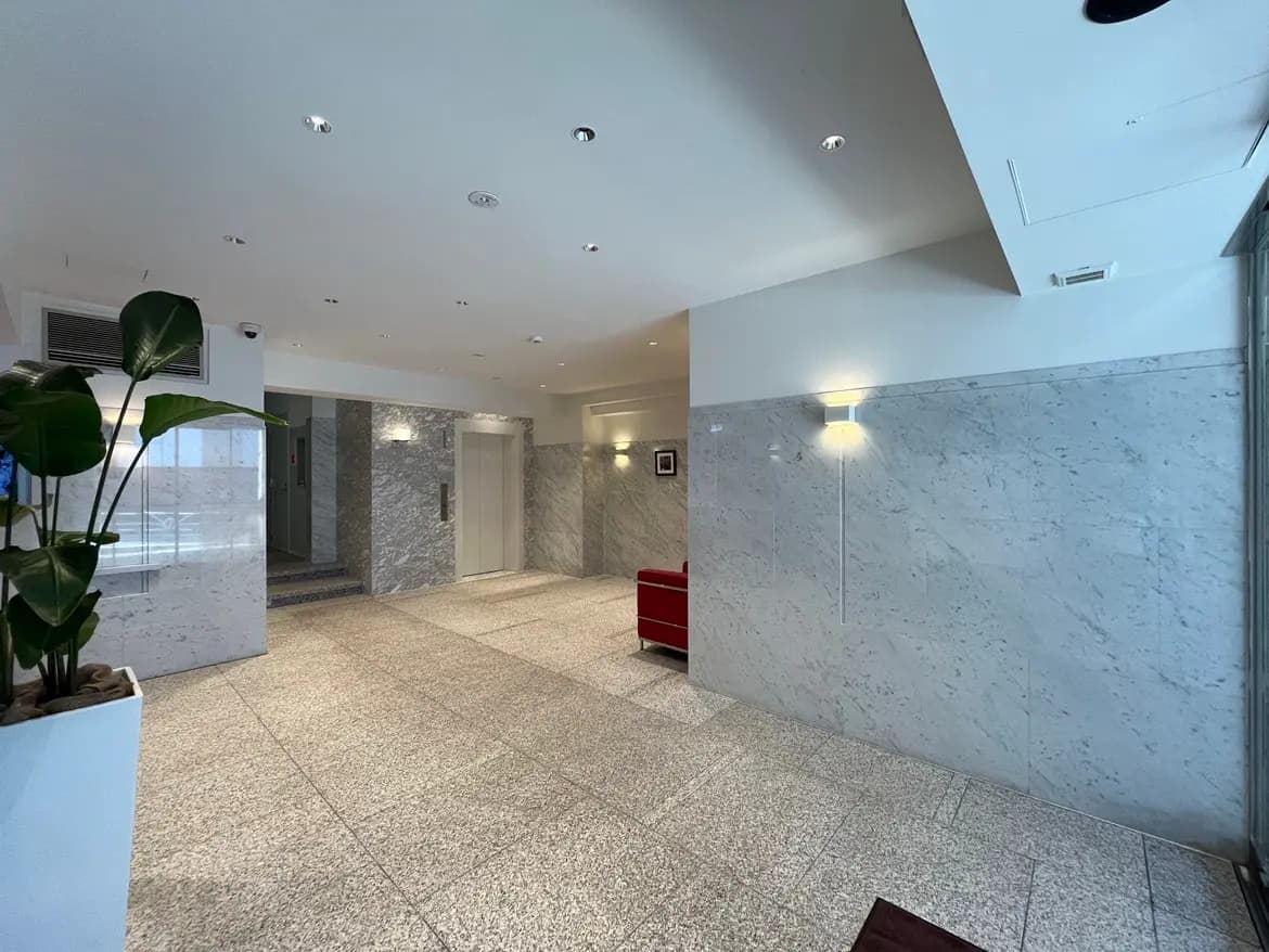 - 石材の壁と広々とした床を持つ現代的なエントランスホール、エレベーターと観葉植物が配置された明るい空間