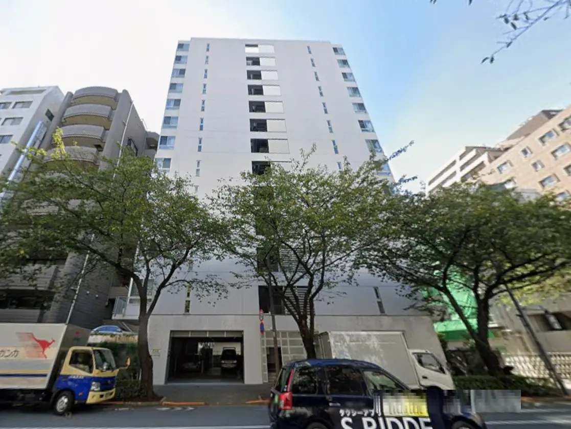 - 近代的なデザインの高層マンション、周囲に緑の木々と駐車スペースが見える外観の写真