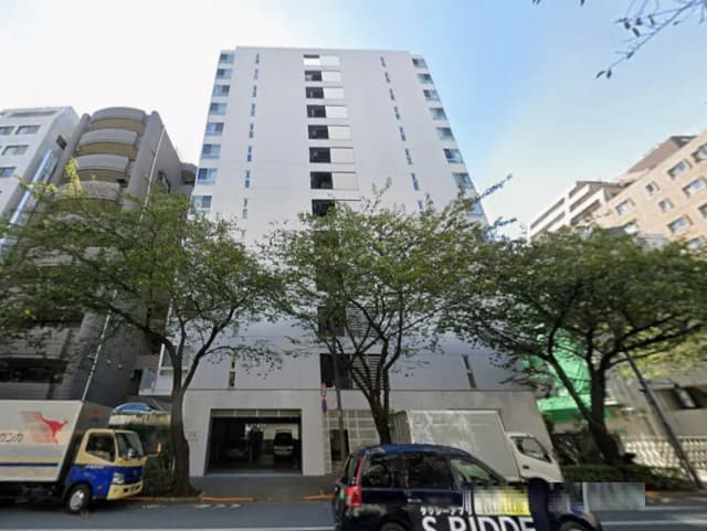 - 近代的なデザインの高層マンション、周囲に緑の木々と駐車スペースが見える外観の写真