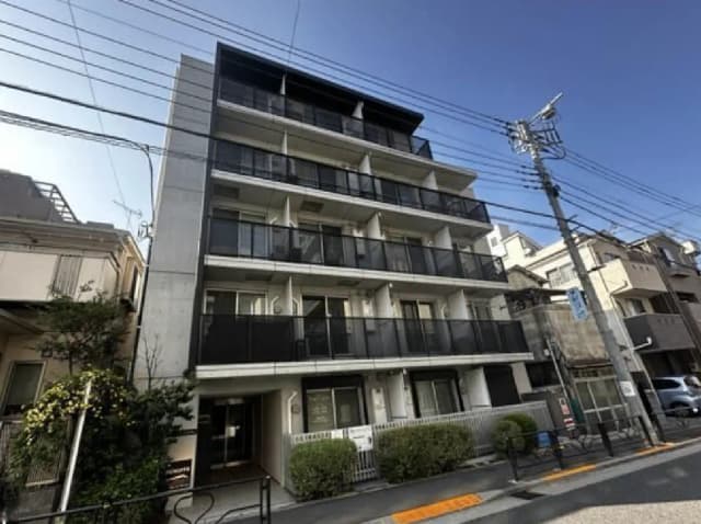 - モダンな外観の4階建てアパートメント、バルコニー付きで周囲には小さな庭木が配置されている様子