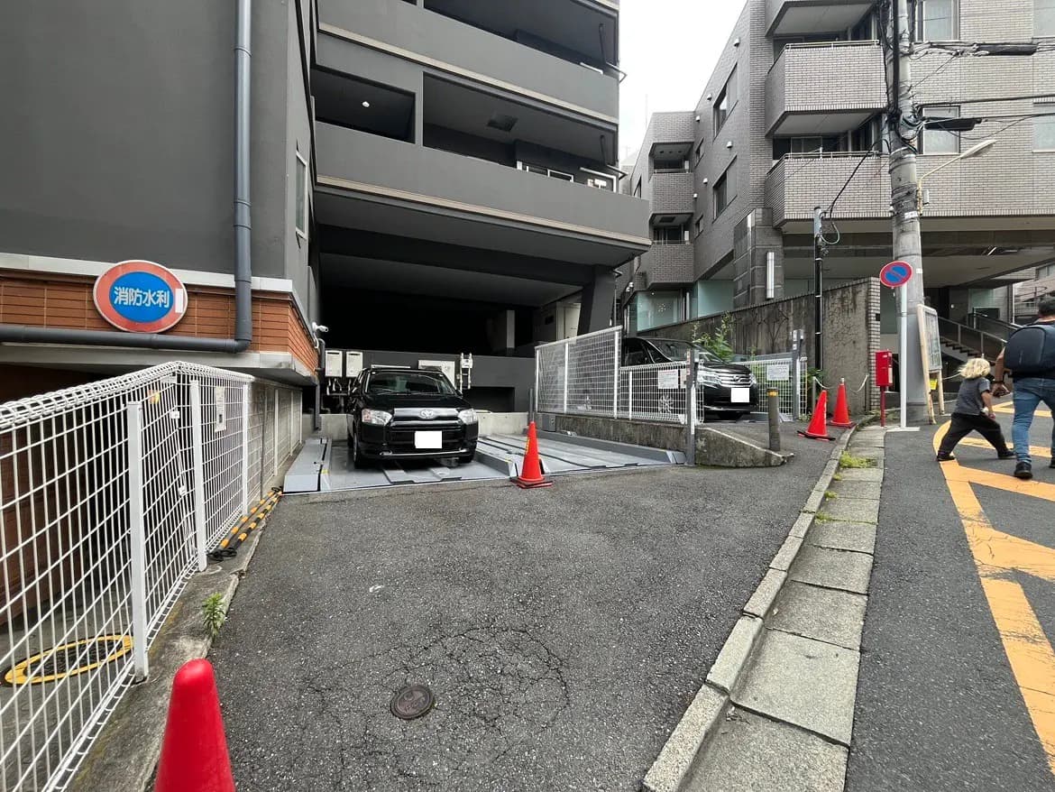 - 住宅ビルの内部駐車場入口、黒い車が停まっている様子、赤いコーンとフェンスで囲まれた安全対策
