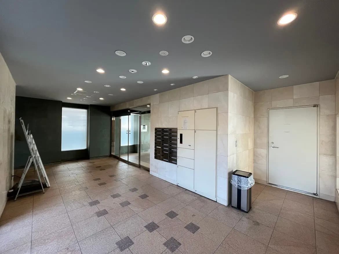 - モダンなデザインのマンションのエントランス、明るい照明と大きな窓があり、郵便受けとごみ箱が配置されたスペース