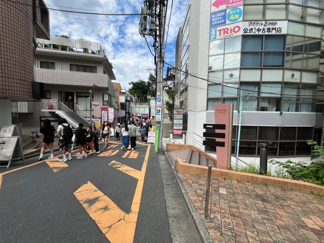 - 多くの人々が行き交う賑やかな街並み、K-POPショップの看板がある道沿いの風景
