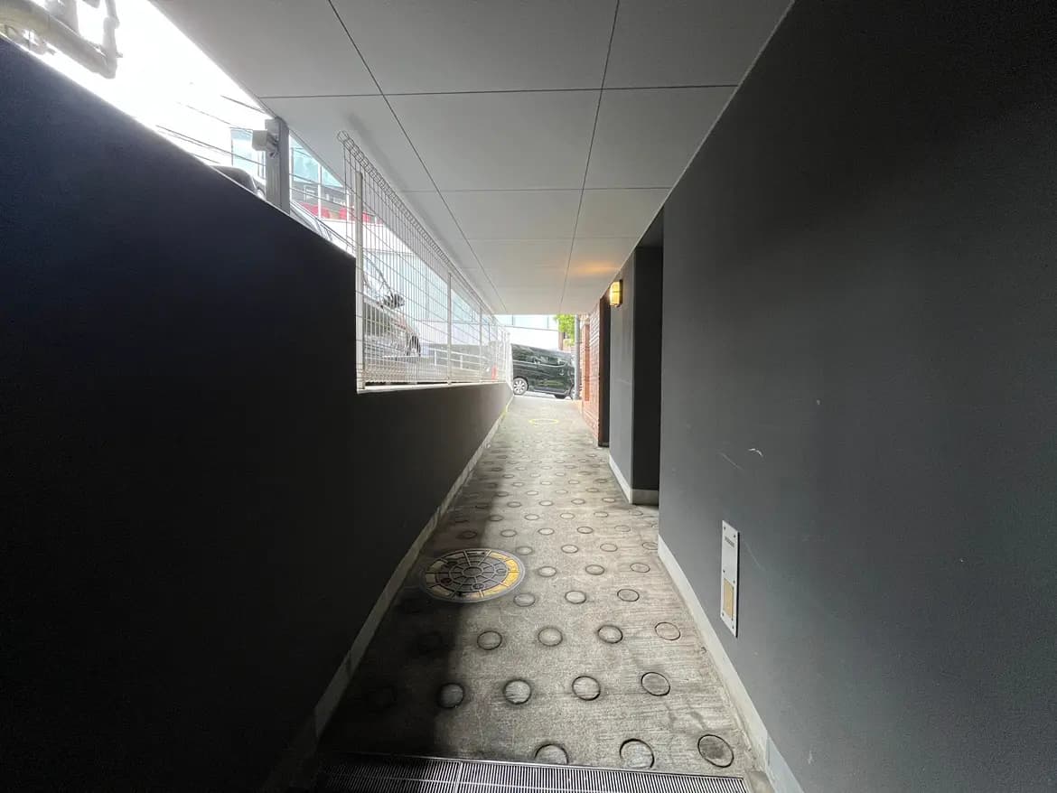 - 現代的なデザインの狭い通路、黒い壁と明るい照明が特徴、舗装された床に円形の模様が散見される