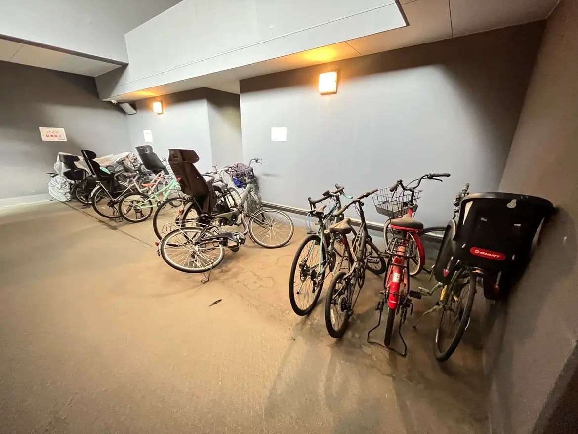 - 屋内の自転車置き場、整理された自転車が並び、壁はグレーで明るい照明が設置されている様子