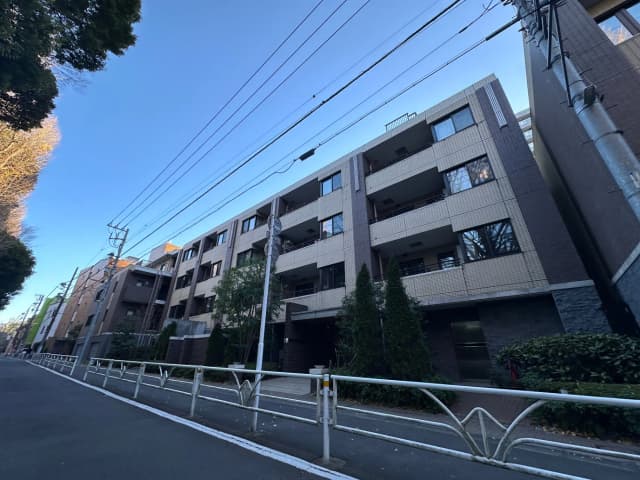 道路沿いに建つ現代的なマンション、タイル張りの外壁とベランダ、青空と都市の景観