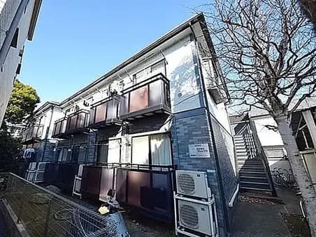 - 笹やかな青空の下にあるアパートメントビル、バルコニー付きの部屋が並び、隣接する階段と街路樹が見える景観