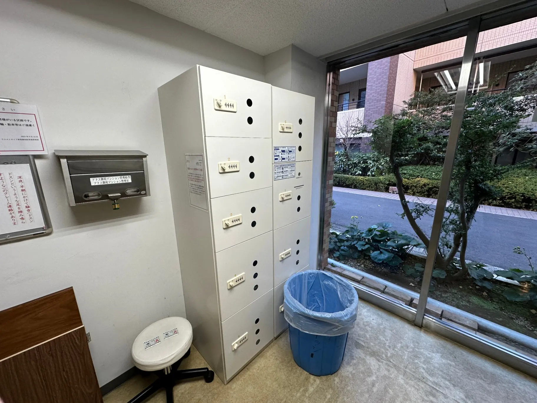 室内の郵便受けと多目的に使用できるチェア、窓越しに見えるマンションの緑豊かな庭園