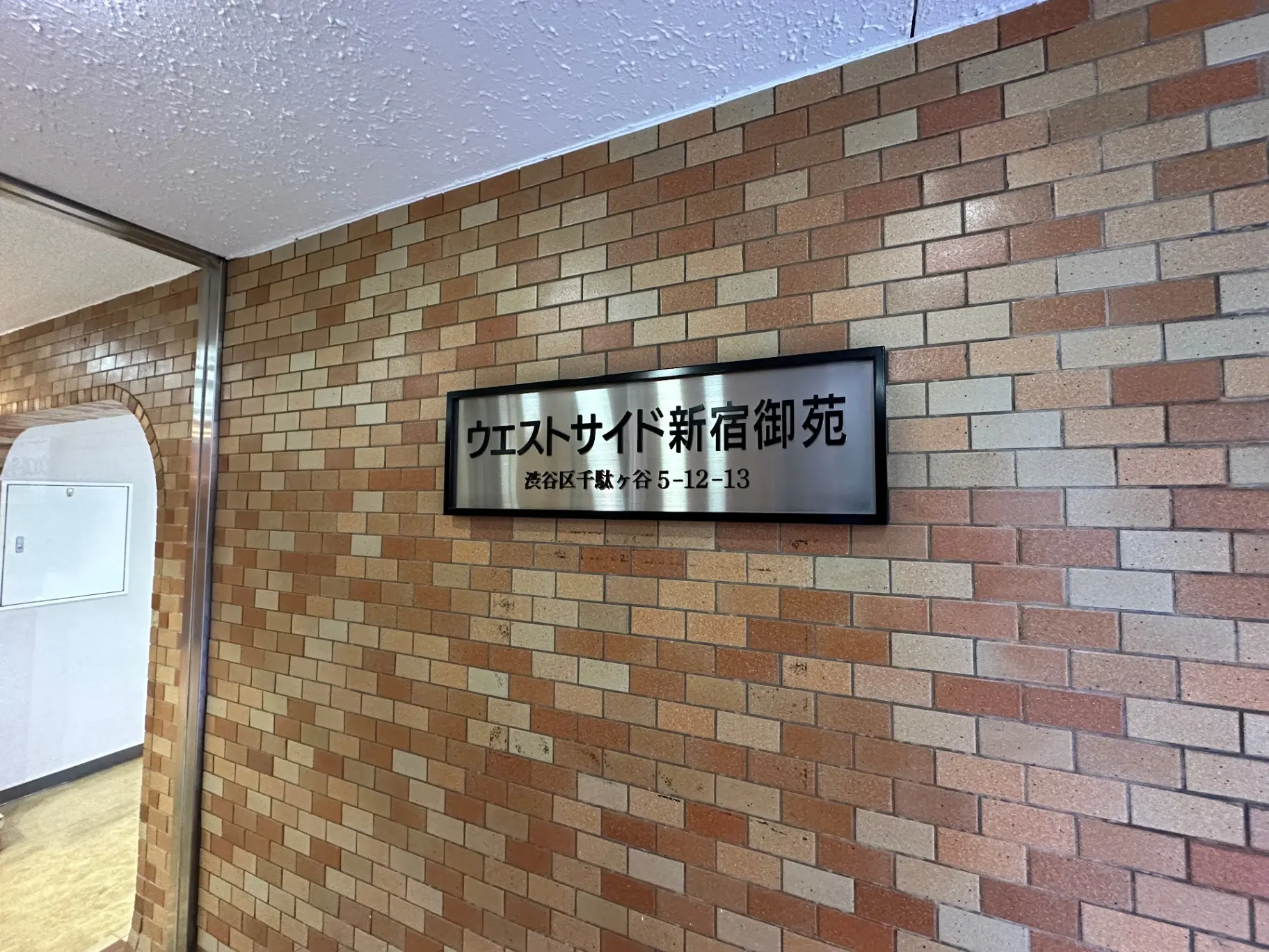 ブリックタイル壁に取り付けられたオフィスサイン、通り抜け可能なアーチ型の通路が見えるオフィス入口