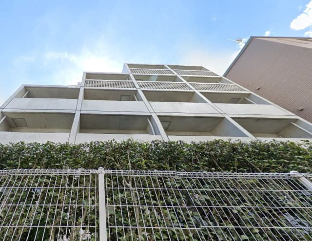 コンクリート製の外壁が特徴の現代的なマンション外観、青空と緑の植物が映える景観