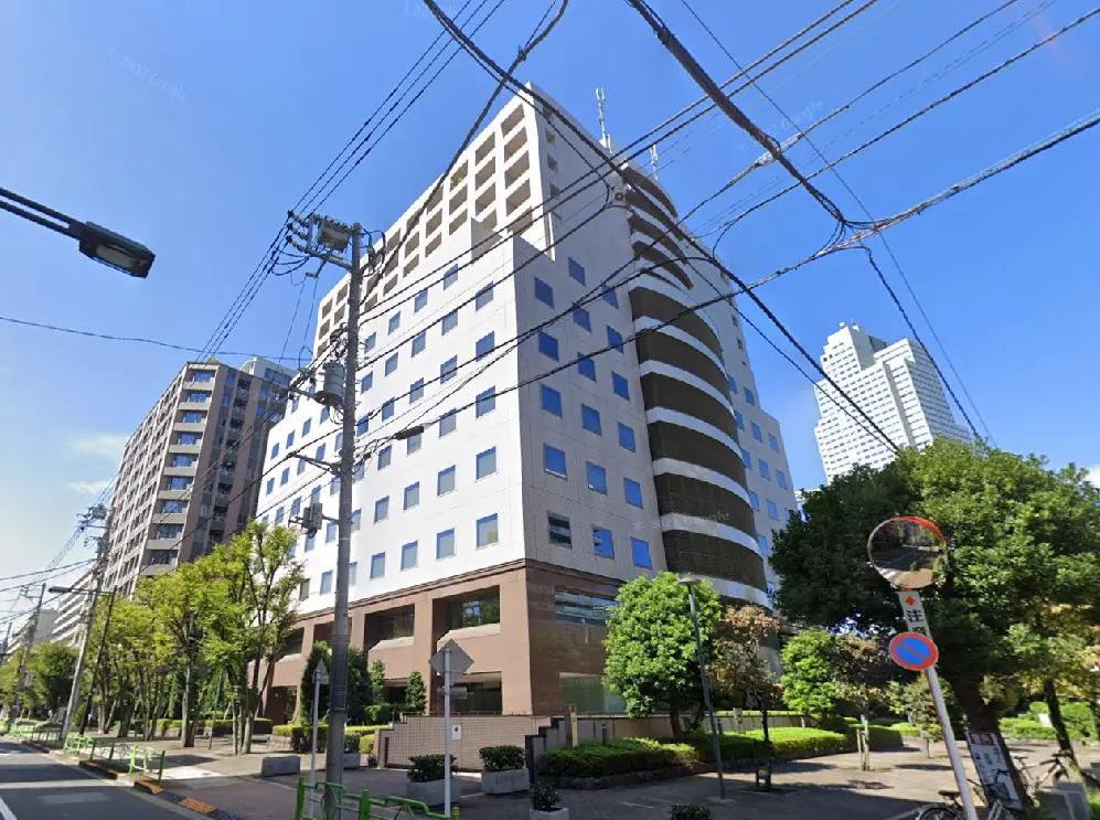 - 都市部のオフィスビル、近隣に高層マンションと緑豊かな街路樹が広がる風景、青空の下でリラックスした雰囲気
