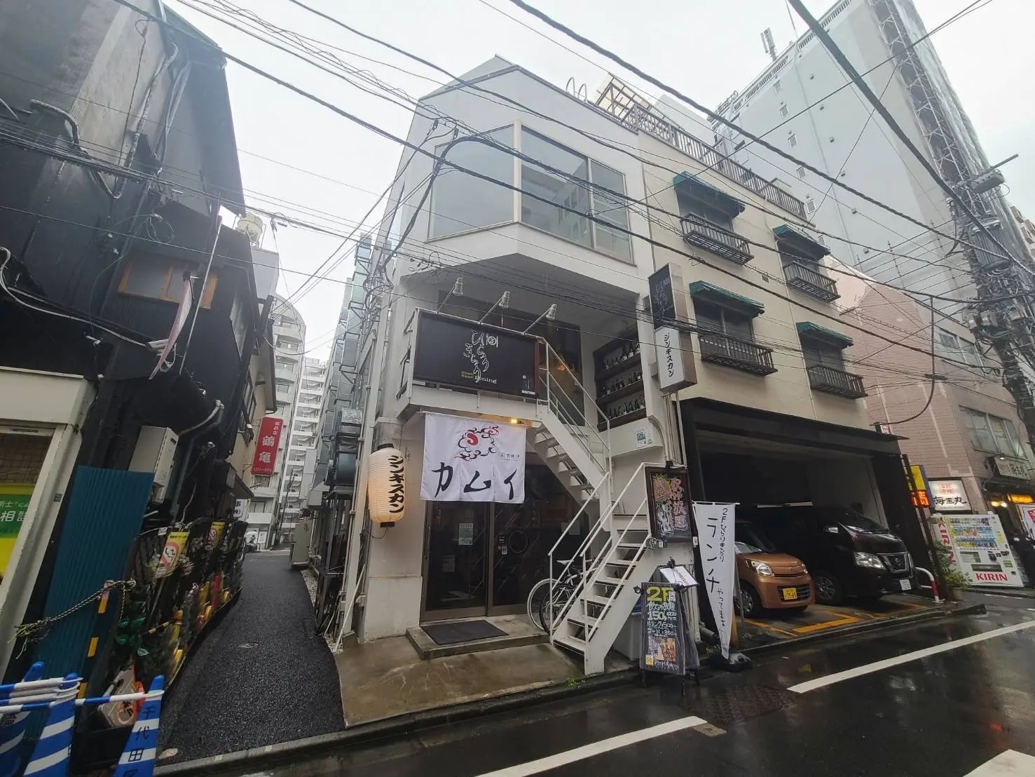 狭い通りに建つ多階層のビル、外階段と店舗の看板が見える都市風景